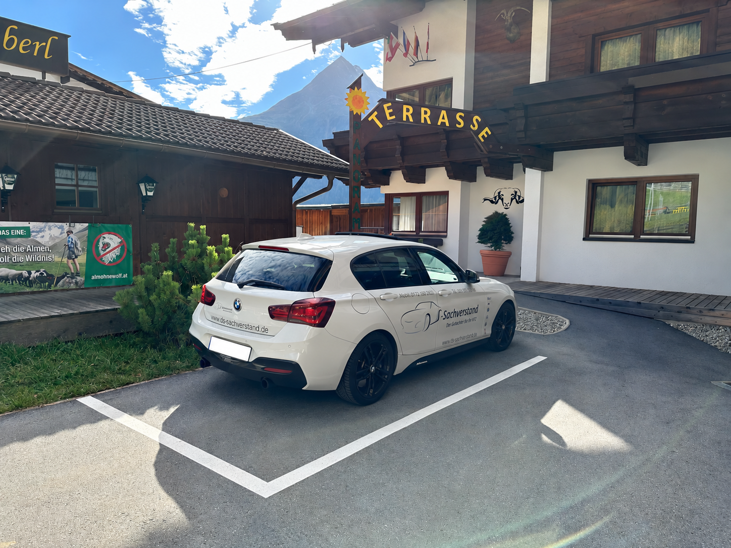 Weißer BMW 1er des Kfz-Gutachters Dirk Steffen mit DS-Sachverstand-Beschriftung parkt vor einem Hotel mit Terrasse